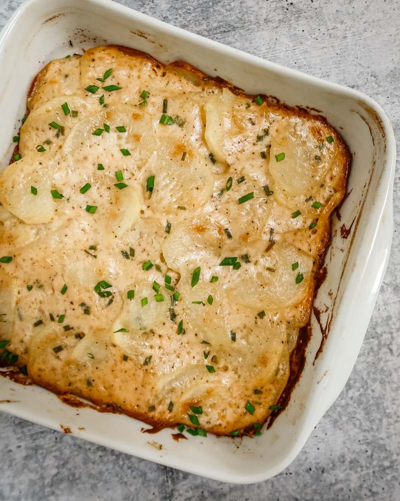 Baking dish with scalloped potatoes ganished with chives.