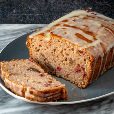 Cranberry sauce bread on a plate with one slice in front.