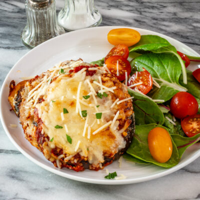 An eggplant parmesan serving on a plate with salad.