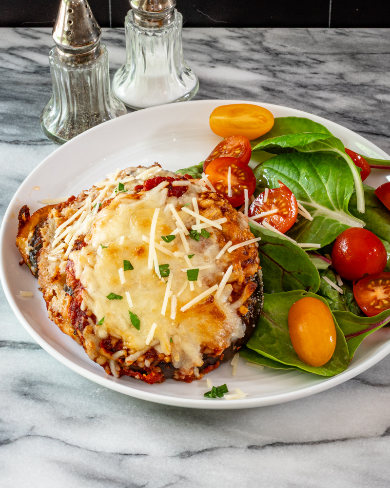 An eggplant parmesan serving on a plate with salad.