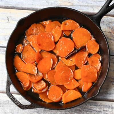 An iron skillet with sweet potatoes and a cinnamon stick.