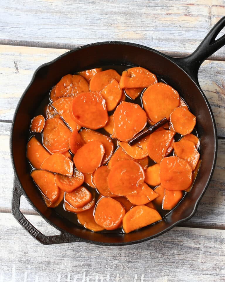 An iron skillet with sweet potatoes and a cinnamon stick.