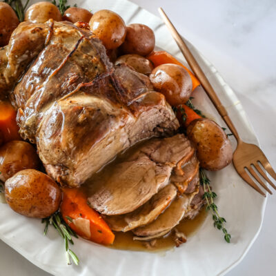 A roast leg of lamb with gravy on a platter with vegetables
