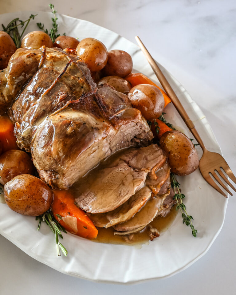 A roast leg of lamb with gravy on a platter with vegetables