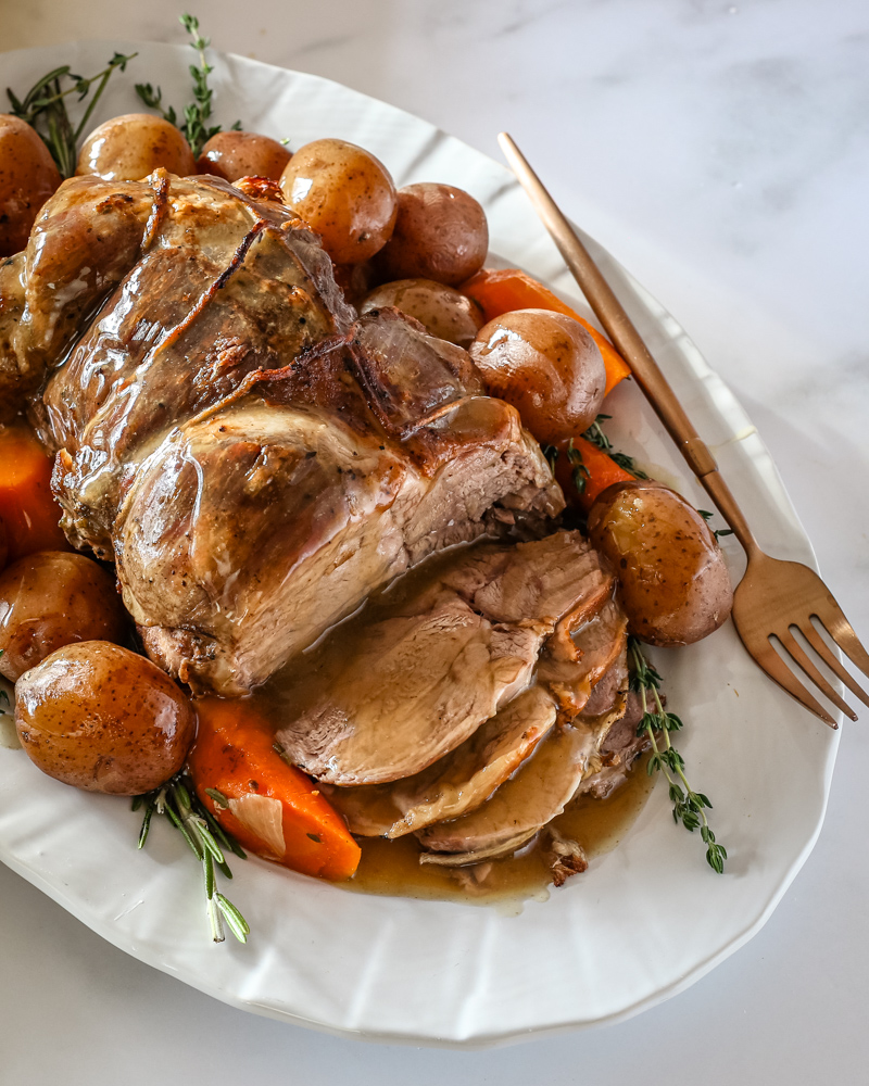 A roast leg of lamb with gravy on a platter with vegetables