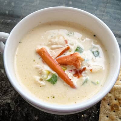 A cup of lobster stew with a few saltine crackers on the side.