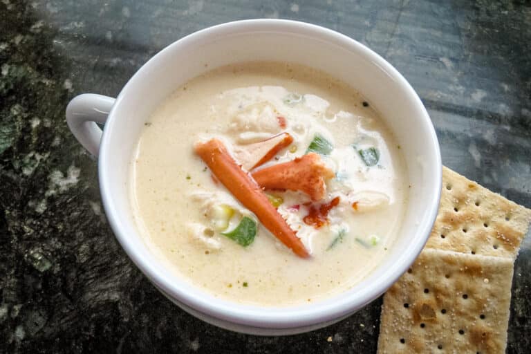 A cup of lobster stew with a few saltine crackers on the side.