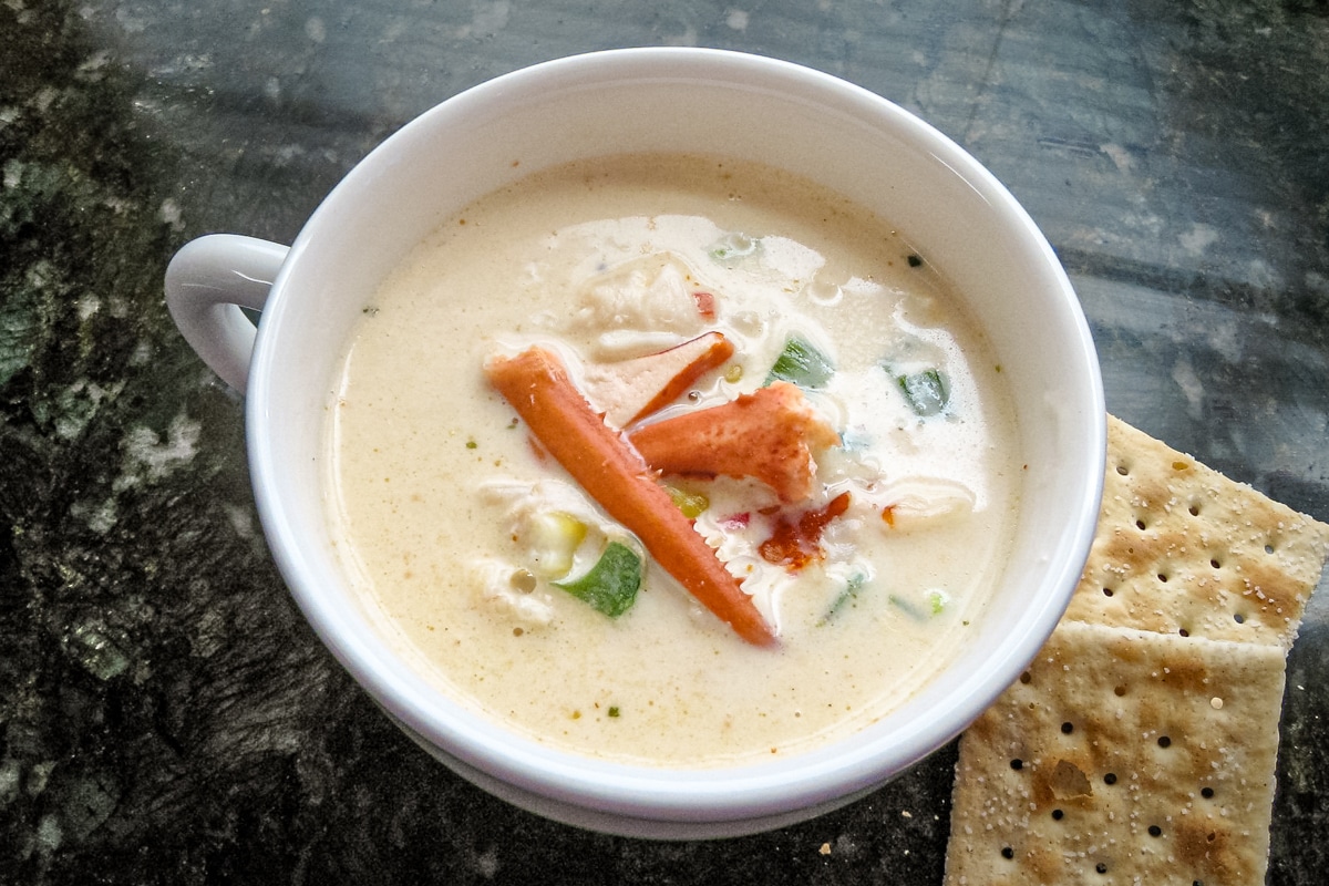 A cup of lobster stew with a few saltine crackers on the side.