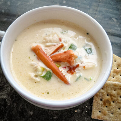 A cup of lobster stew with a few saltine crackers on the side.