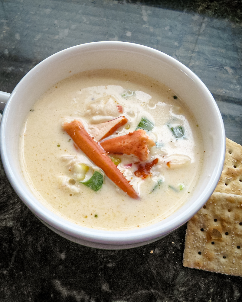 A cup of lobster stew with a few saltine crackers on the side.