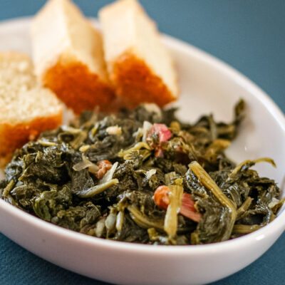 A dish of mustard greens with bacon and sliced cornbread