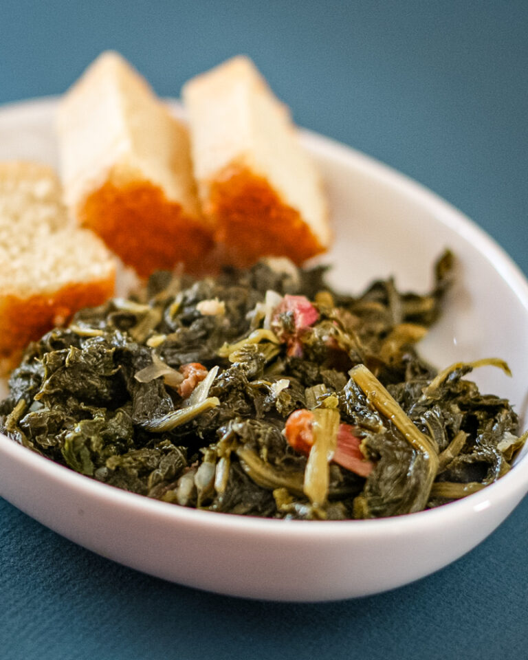 A dish of mustard greens with bacon and sliced cornbread