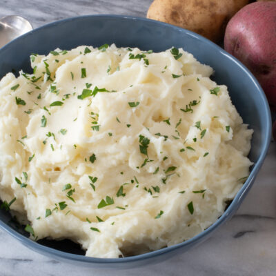 Mashed potatoes in a blue bowl with some parsley for garnish.