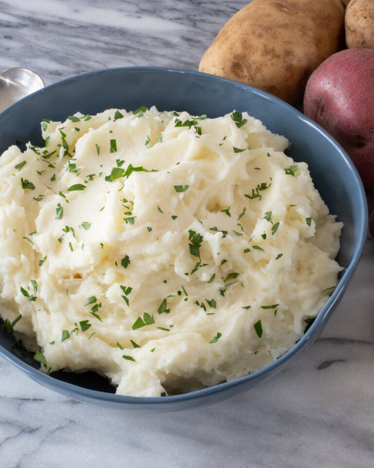 Mashed potatoes in a blue bowl with some parsley for garnish.