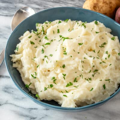 Mashed potatoes in a blue bowl with some parsley for garnish.