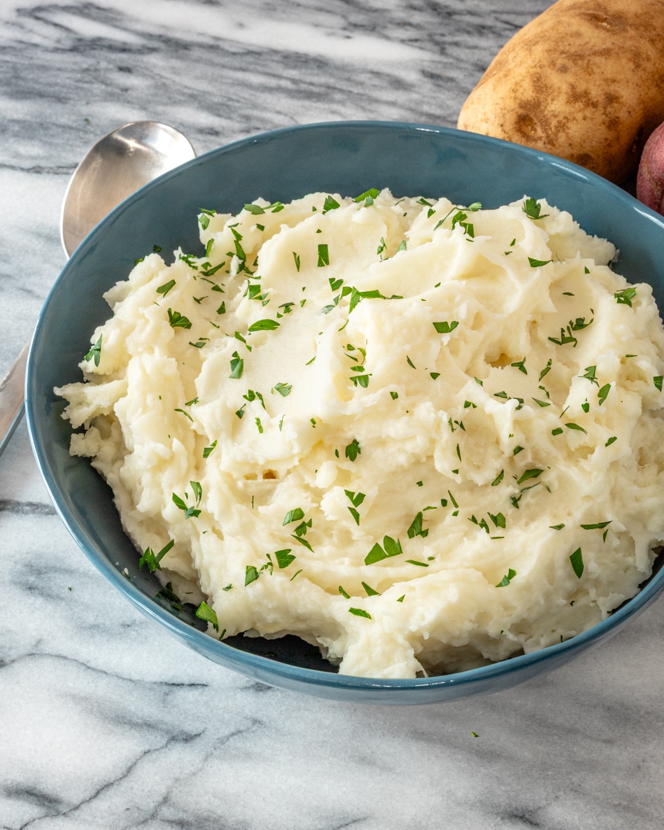 Mashed potatoes in a blue bowl with some parsley for garnish.