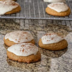 Iced pumpkin cookie with more on a rack behind them.