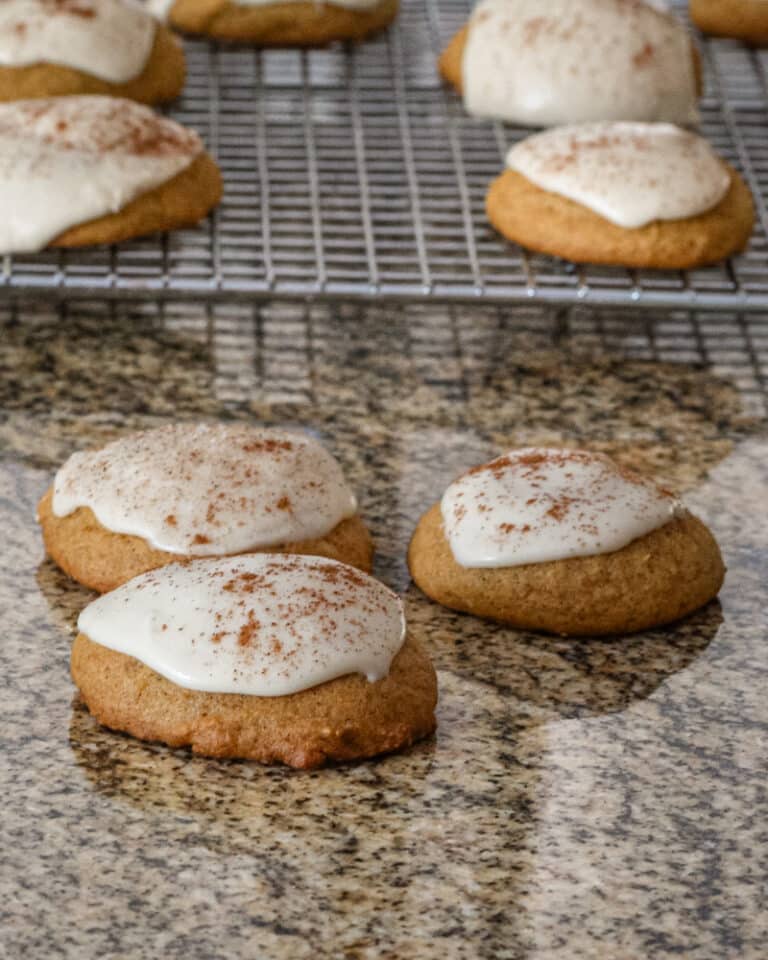 Iced pumpkin cookie with more on a rack behind them.