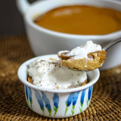 A ramekin with pumpkin pudding, showing a spoon lifting some of the pudding out.