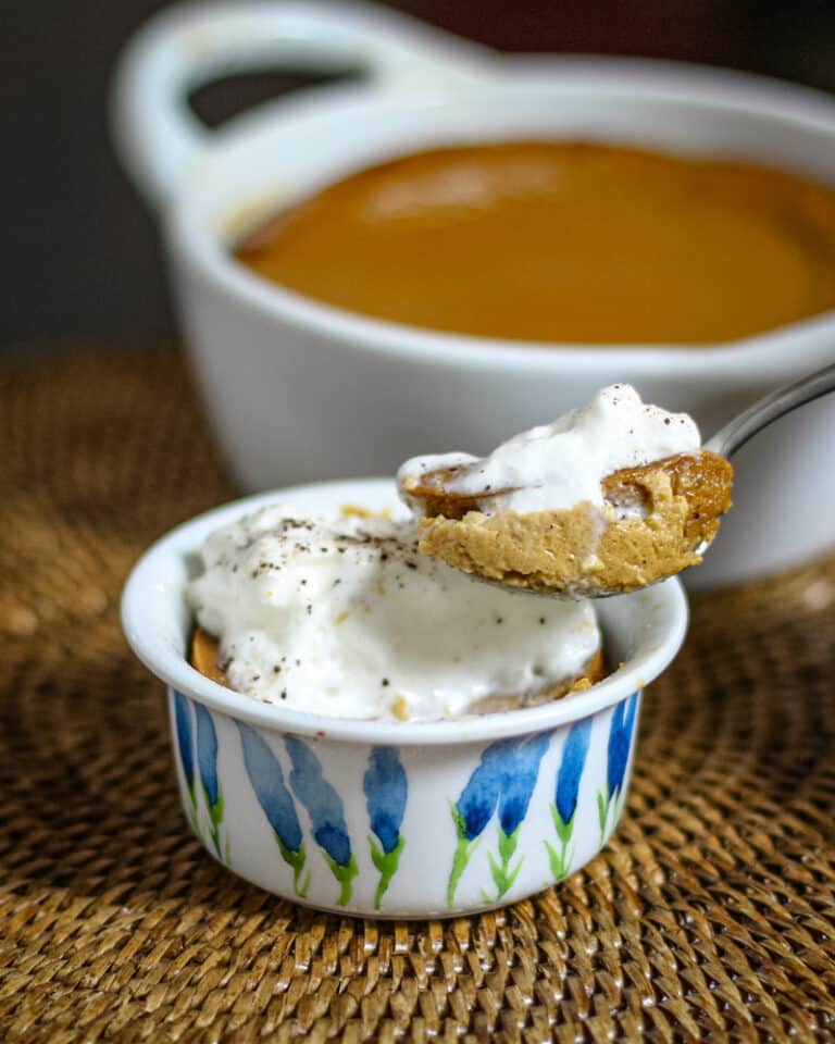 A ramekin with pumpkin pudding, showing a spoon lifting some of the pudding out.