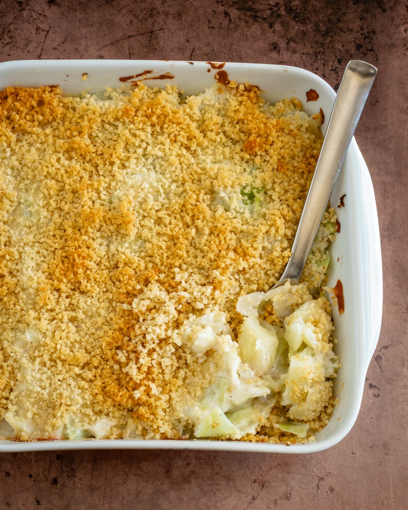 A baking dish with scalloped cabbage, served with a large spoon.