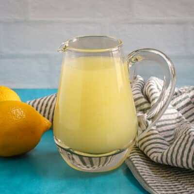A small pitcher of lemon sauce for desserts with lemons in the background.