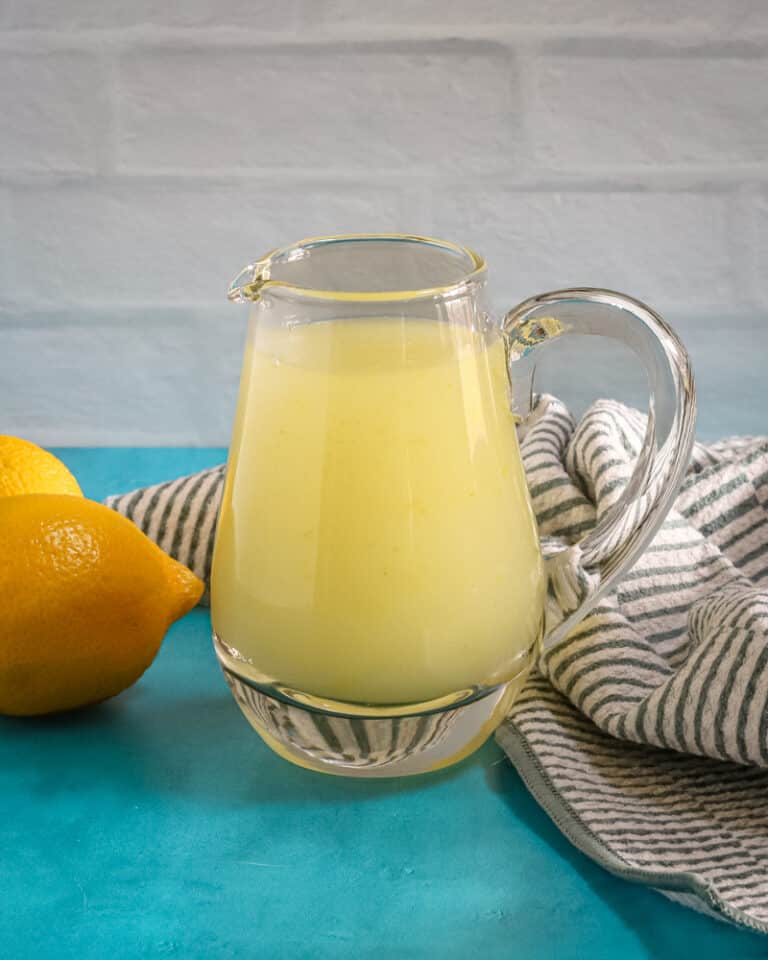 A small pitcher of lemon sauce for desserts with lemons in the background.