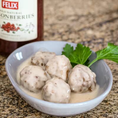 A small bowl of Swedish meatballs with lingonberry jam in the background.