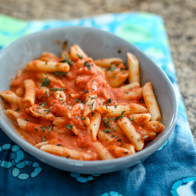 Pasta with tomato sauce and fresh herbs in a gray bowl.