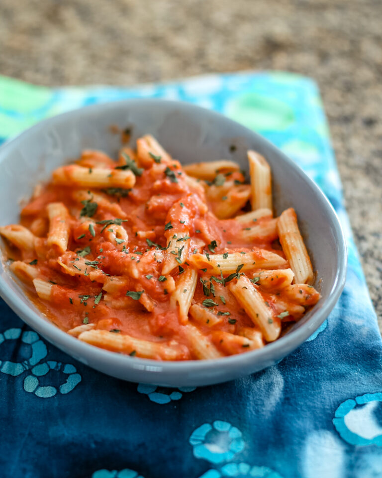 Pasta with tomato sauce and fresh herbs in a gray bowl.
