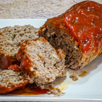 A tasty loaf of cheddar and tomato soup meatloaf on a platter, sliced.