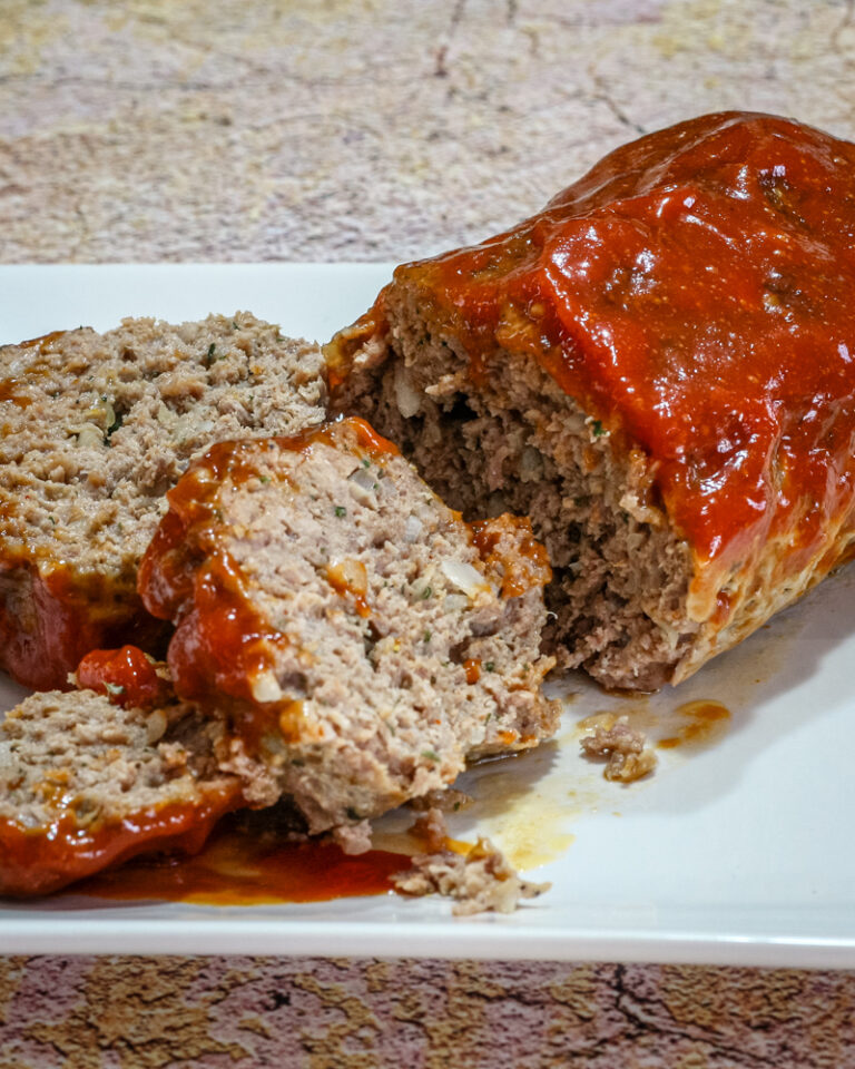A tasty loaf of cheddar and tomato soup meatloaf on a platter, sliced.