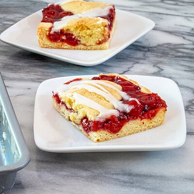 Slices of cherry cobbler bats on dessert plates with a baking sheet alongside them.