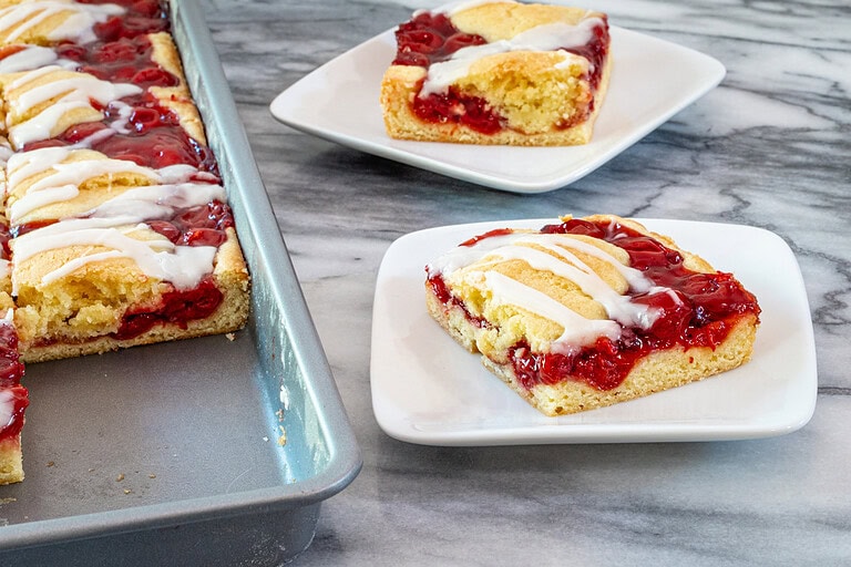 Slices of cherry cobbler bats on dessert plates with a baking sheet alongside them.