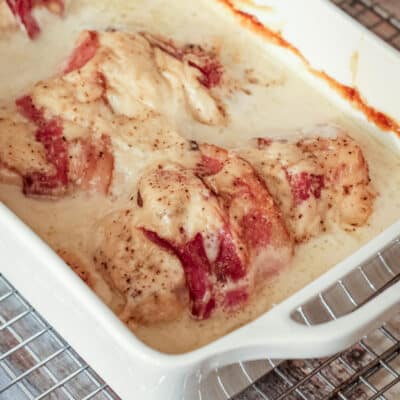 Chicken rolls in a casserole dish wrapped in bacon and baked in a creamy sauce.