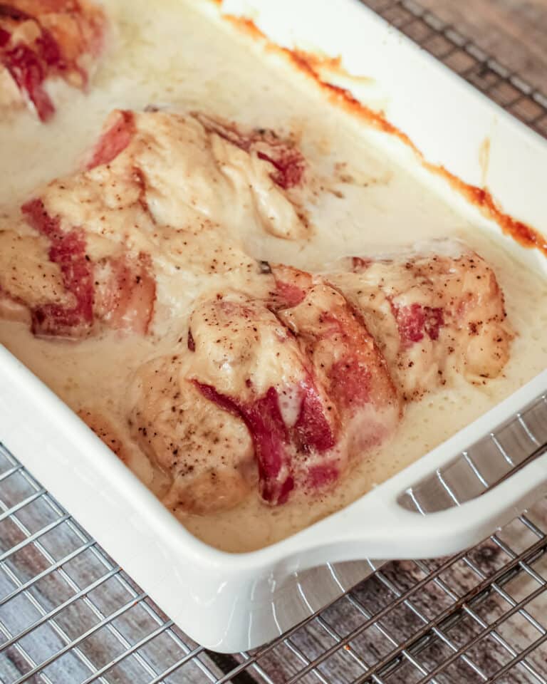 Chicken rolls in a casserole dish wrapped in bacon and baked in a creamy sauce.
