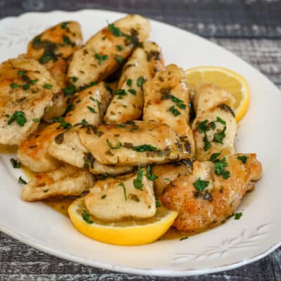 A serving plate of chicken piccata with lemon wedges.