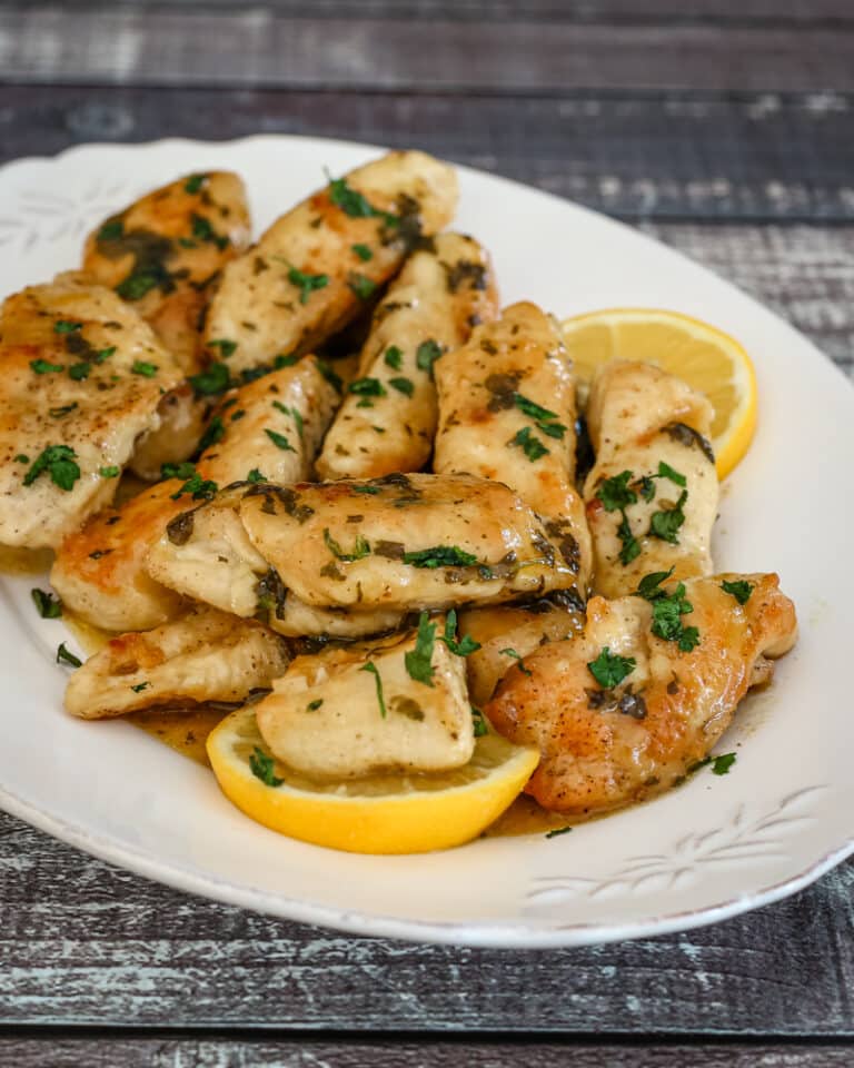 A serving plate of chicken piccata with lemon wedges.