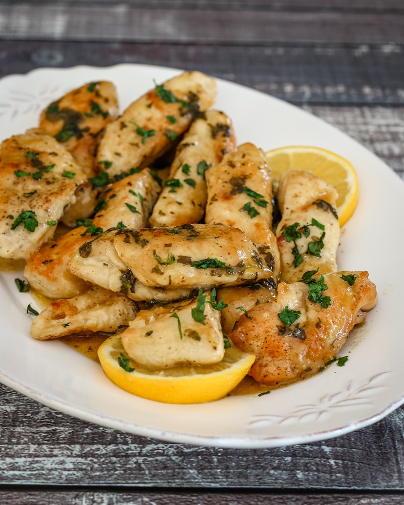 A serving plate of chicken piccata with lemon wedges.