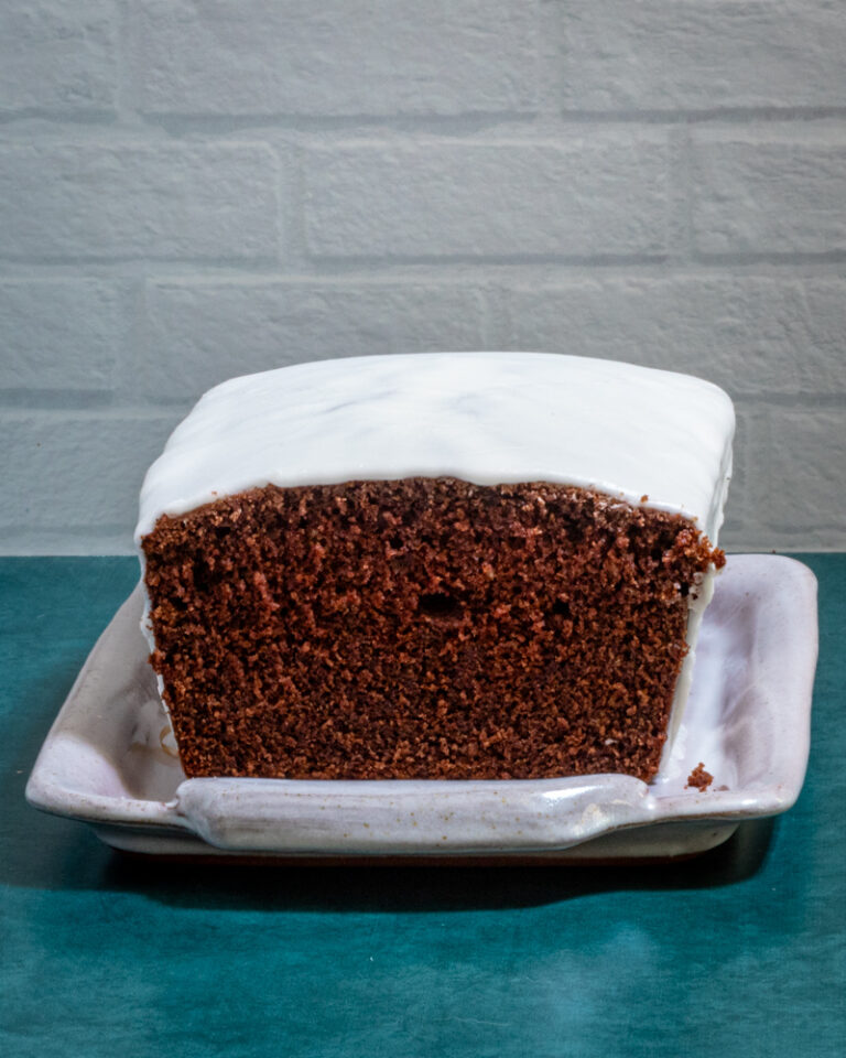An iced chocolate loaf cake on a tray, sliced.