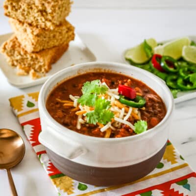 A bowl of turkey chili with garnishes and cornbread in the background.