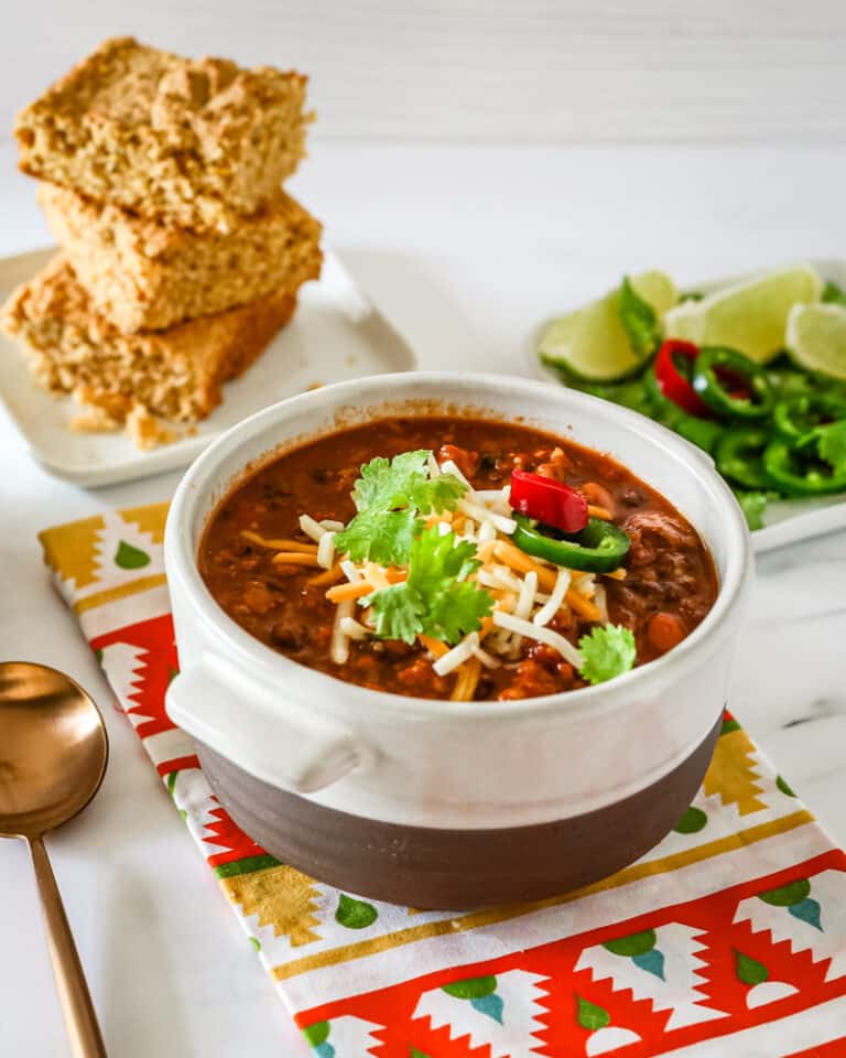 A bowl of turkey chili with garnishes and cornbread in the background.