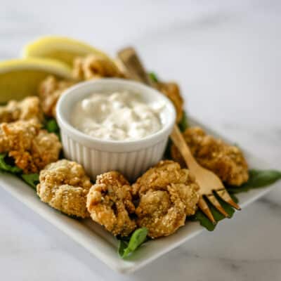 Fried oysters on a plate with tartar sauce and lemon wedges.