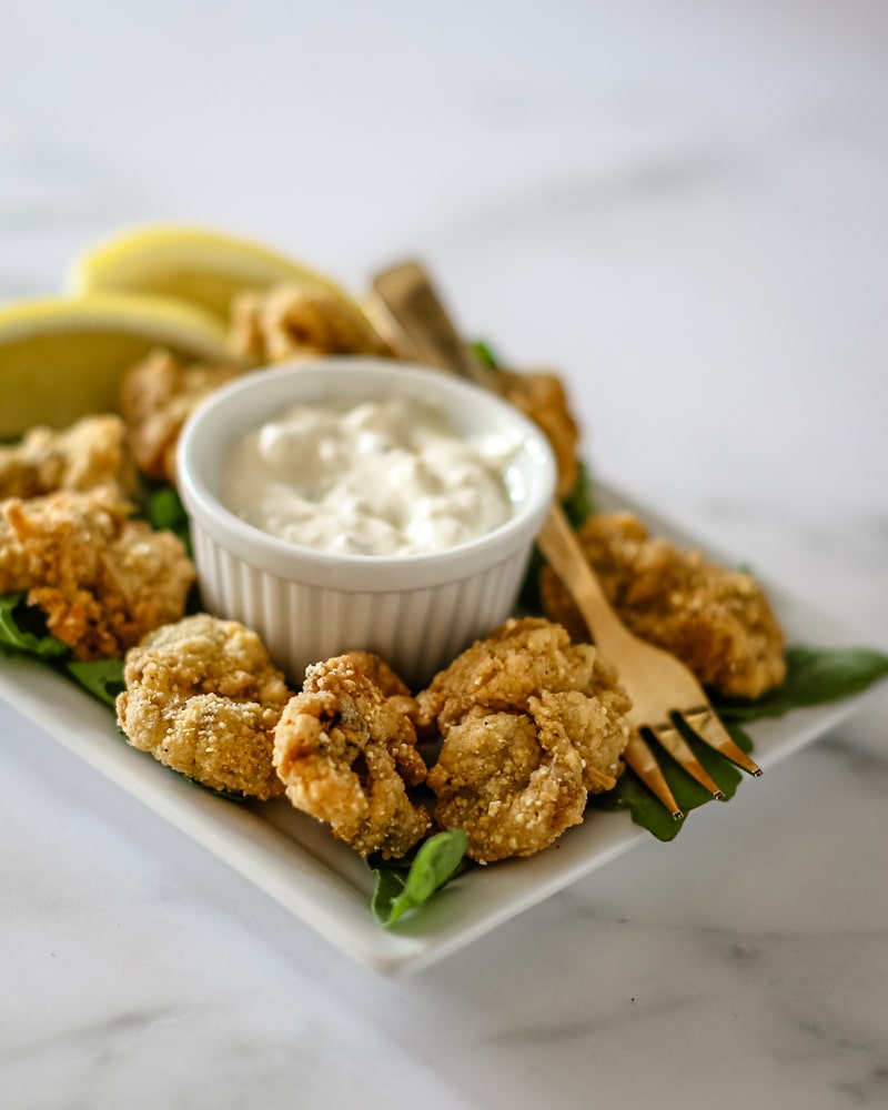 Fried oysters on a plate with tartar sauce and lemon wedges.