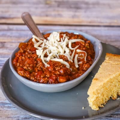 A serving of chili with some cheese and a side of cornbread.