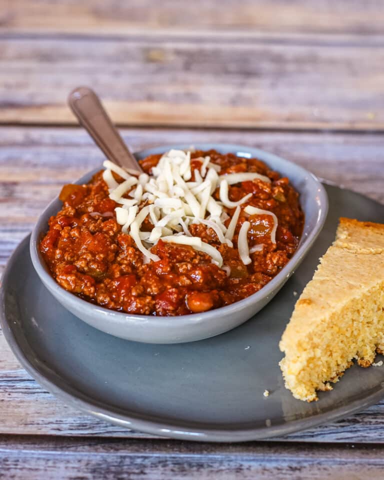 A serving of chili with some cheese and a side of cornbread.