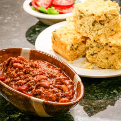 A hearty beef chili with jalapeno cornbread in the background.