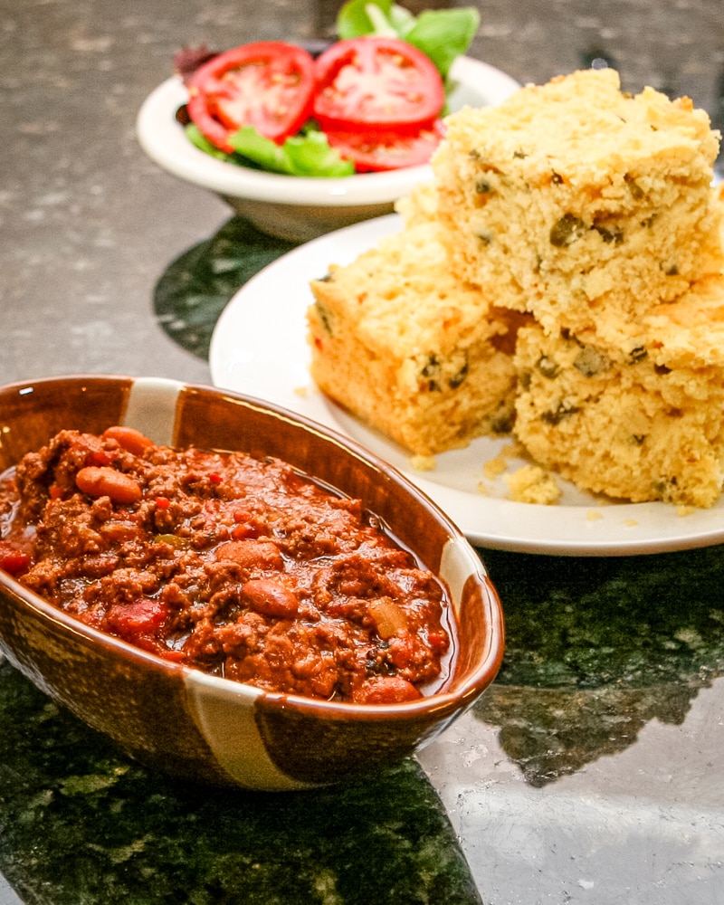 A hearty beef chili with jalapeno cornbread in the background.