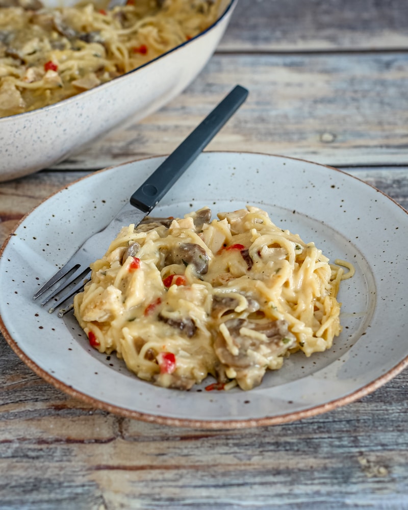 A serving of turkey tetrazzini on a plate with the serving dish behind it.