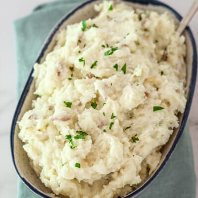 A serving bowl with make-ahead mashed potatoes, garnished with parsley.